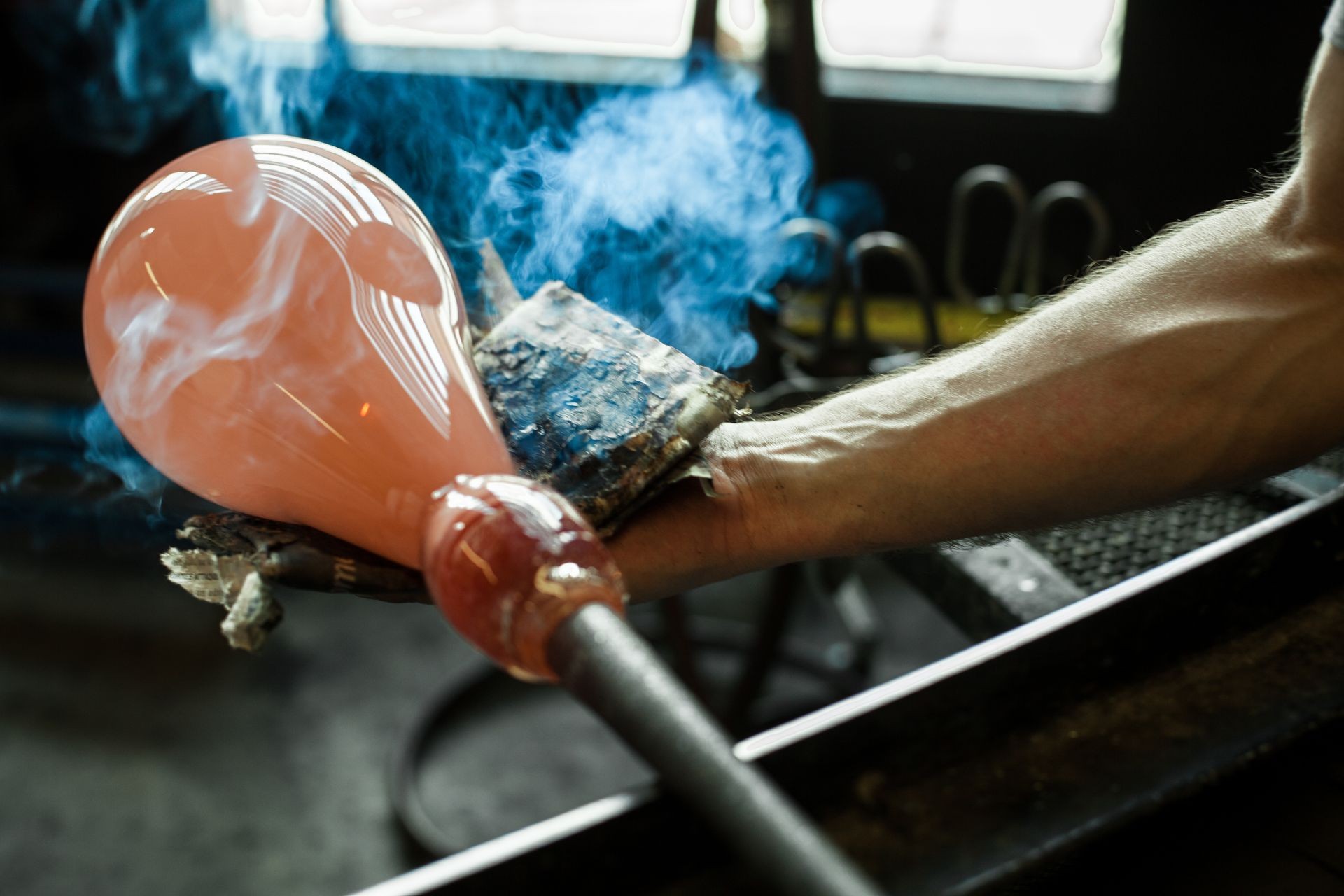 Glass-blower man working with hot ocher glass to make a blown glass lantern